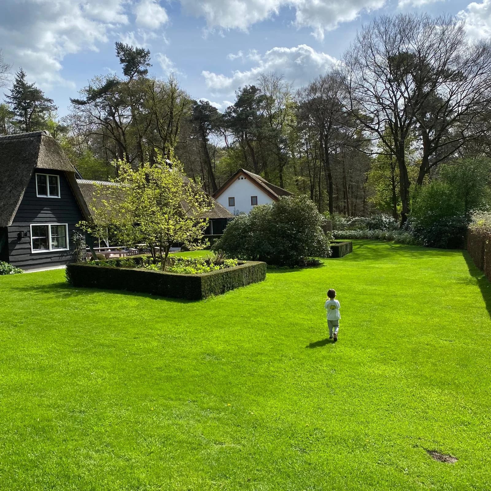 A child walking through a spacious green Dutch garden beside a woodland home
